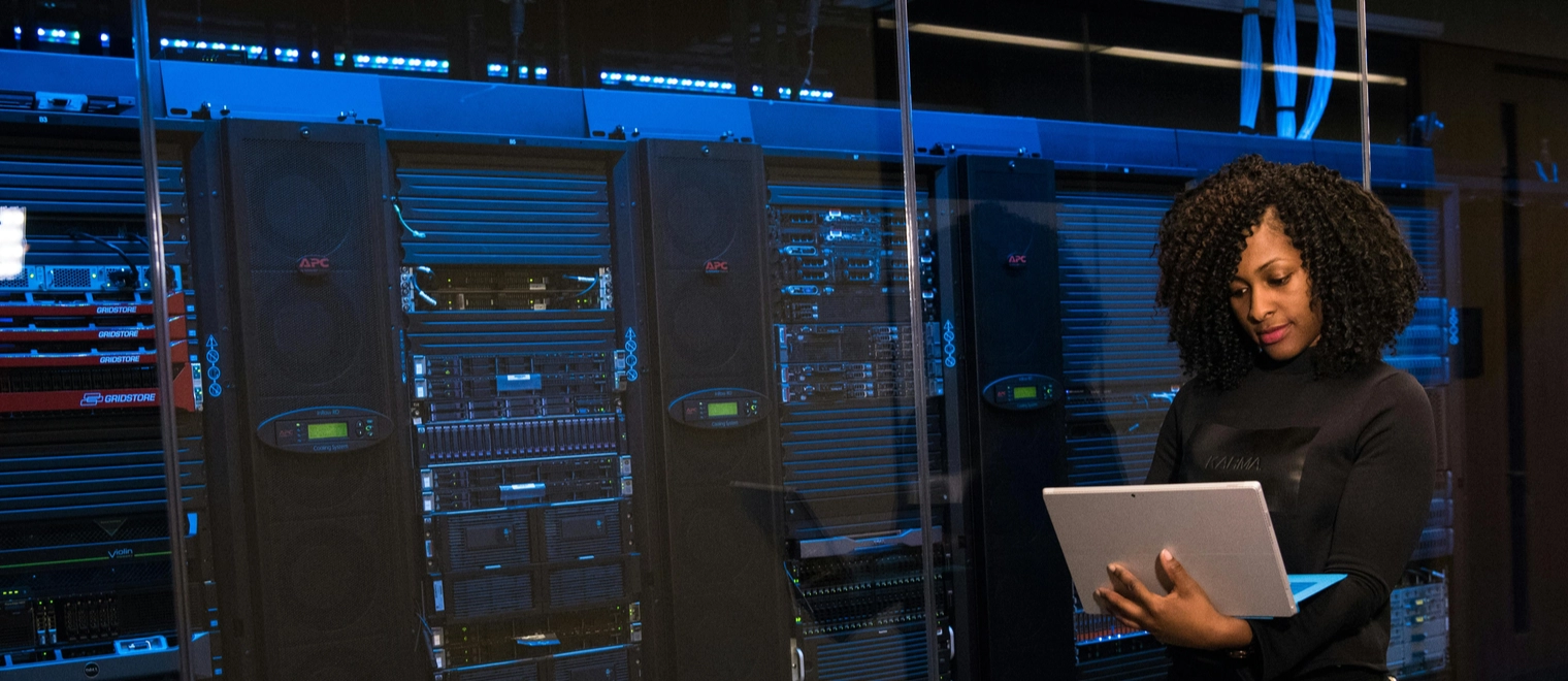 Woman working on laptop in server room.