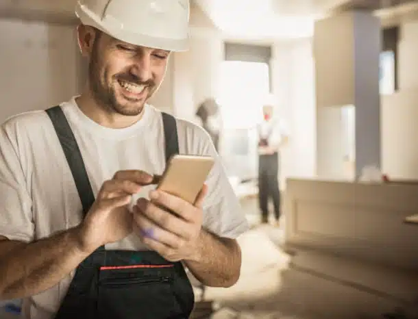 Construction worker smiling while using smartphone indoors