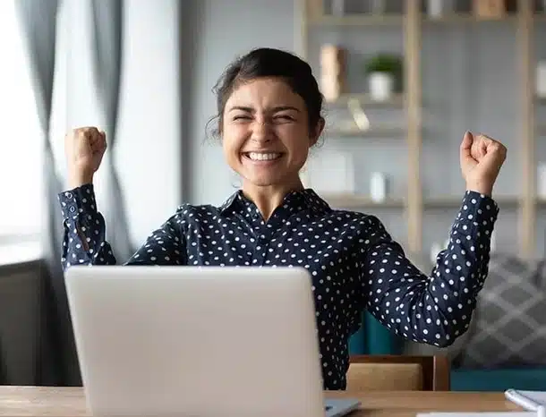 Happy woman celebrating success at computer desk.