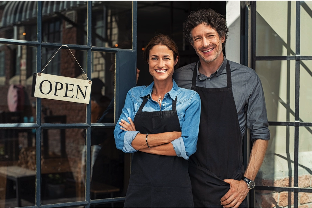 Smiling store owners standing by open sign.